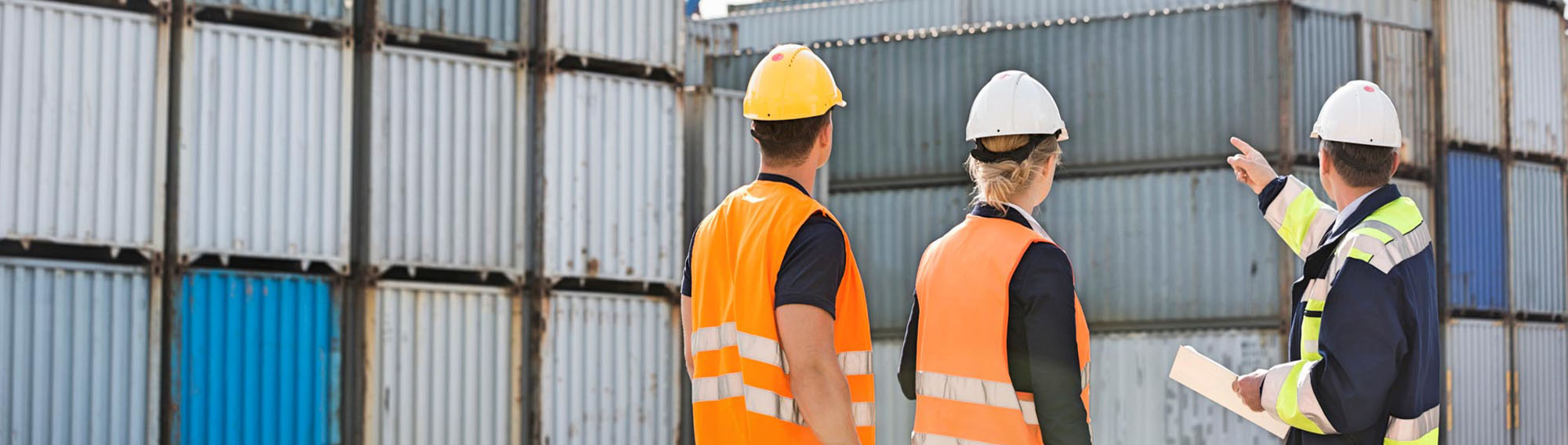 Workers in hard hats pointing at large metal containers.