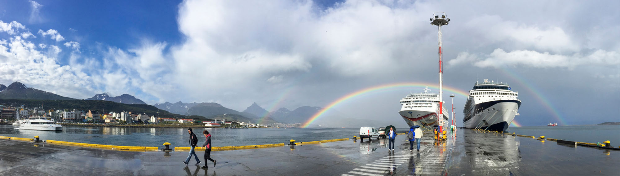 Two ships at a port with a double rainbow behind them.